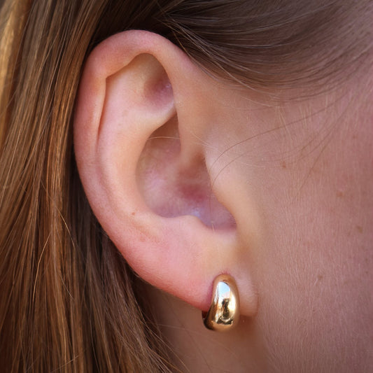 Close-up of a person wearing a gold hoop earring.